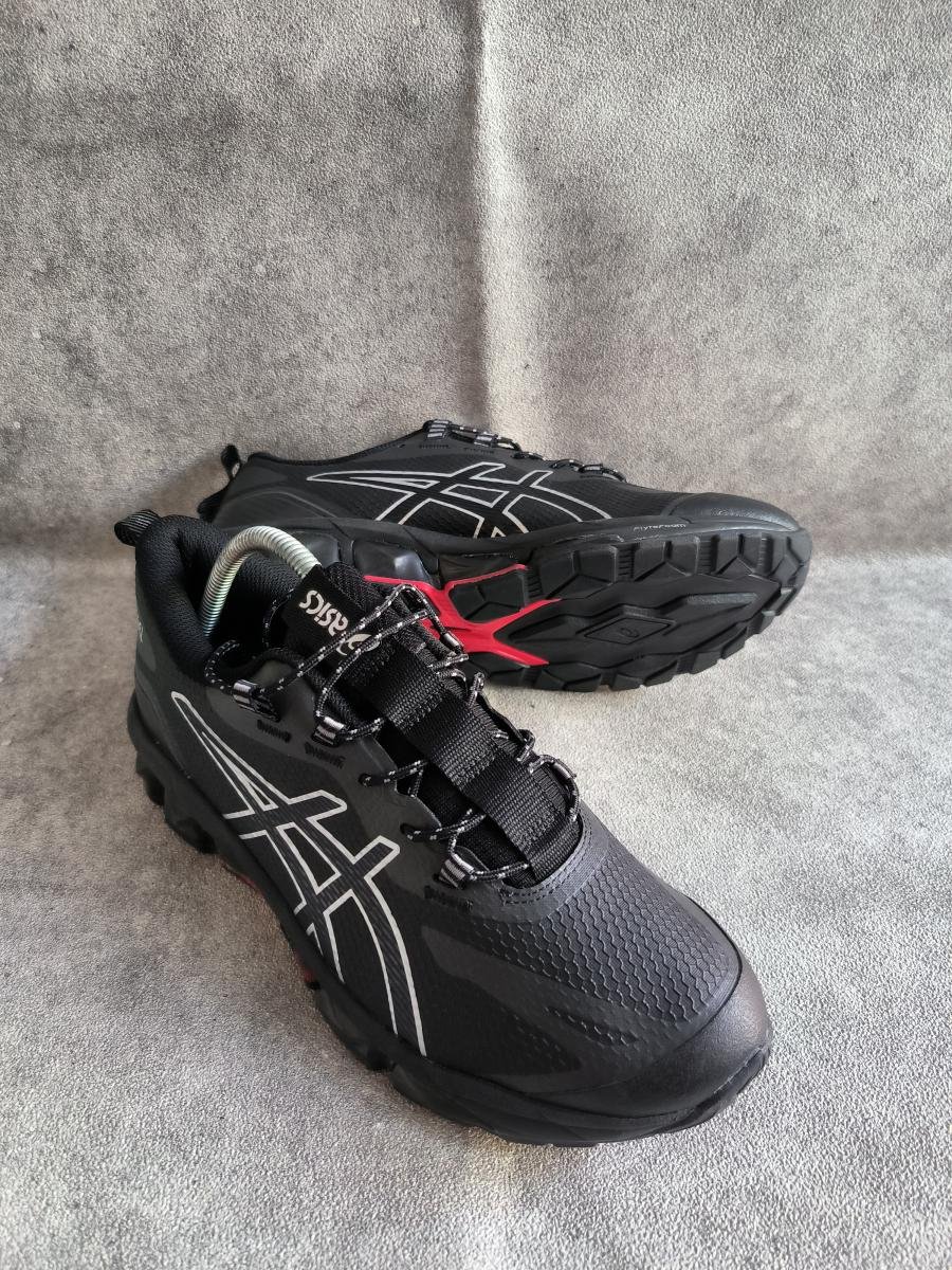 Asics Gel-Quantum 360 VII warna hitam (Black/Graphite Grey) dengan aksen warna merah/oranye di bagian sol bawahnya.
